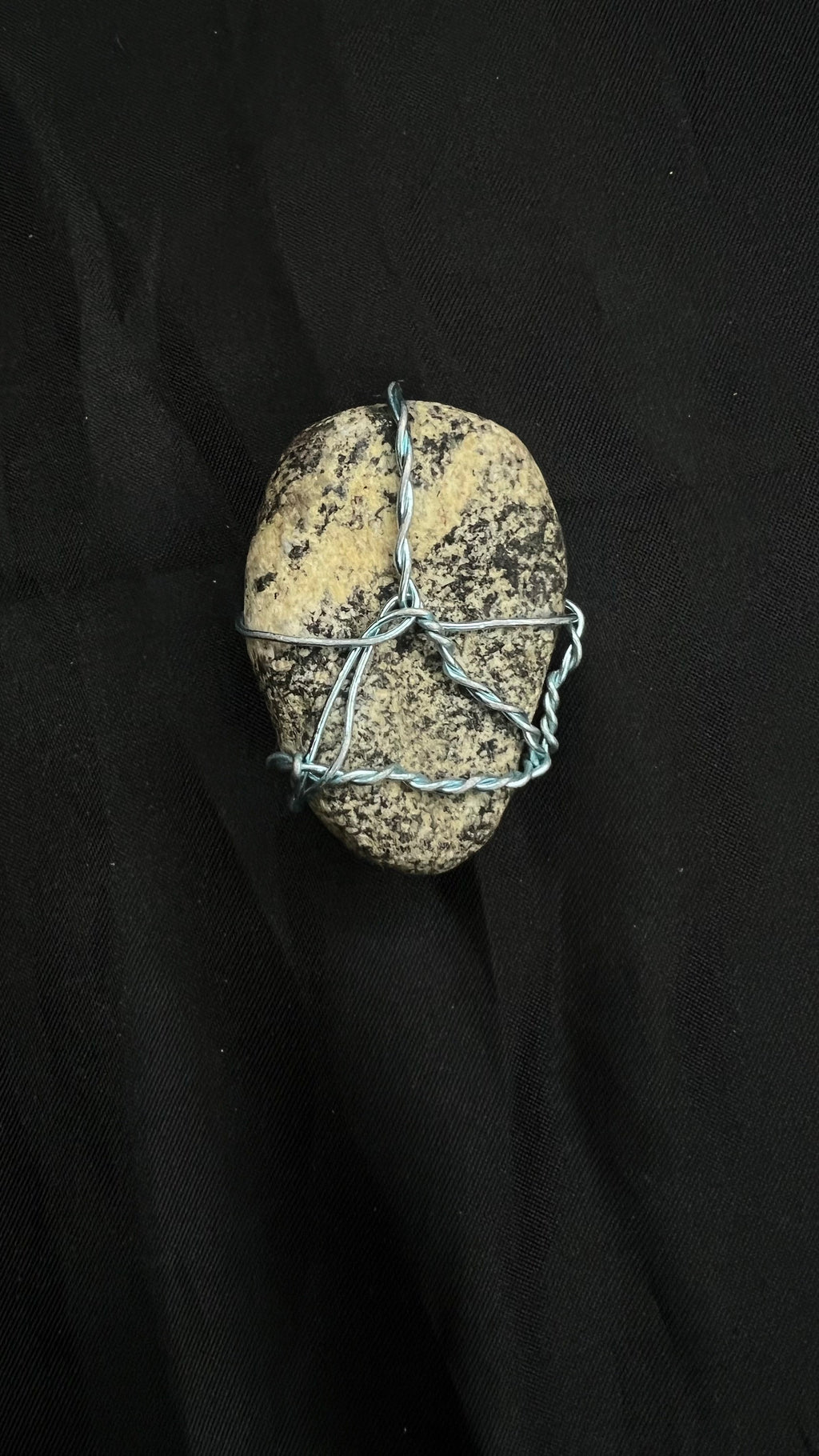 The Speckled Egg — speckled cream river pebble pendant wrapped in silver-tone wire on black cloth
